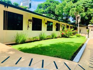 a yellow house with a yard of grass and flowers at Hotel Mango Airport in Alajuela +42 photos
