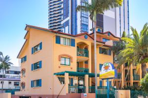 een geel gebouw met palmbomen en hoge gebouwen bij Aruba Sands Resort in Gold Coast