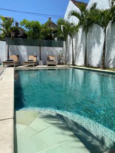 a swimming pool with chairs and palm trees at Villa Oberoi 2 bedrooms in Seminyak