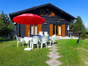 a table and chairs with a red umbrella in front of a house at Chalet Peer Gynt by Interhome in Nendaz