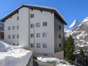 a building in the snow with mountains in the background at Apartment Dianthus-1 by Interhome in Zermatt