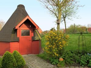 a red doghouse with a black roof in a garden at Apartment Alte Molkerei-1 by Interhome in Friederikensiel
