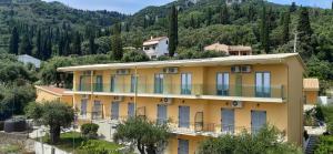 a yellow building with blue windows and a mountain at Passas Mare Apartments & Studios in Benitses