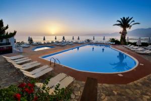 a large swimming pool with lounge chairs and the ocean at Hersonissos Village Hotel & Bungalows in Hersonissos