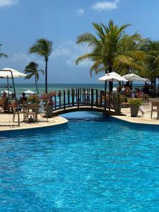 una piscina con un puente y el océano en Apt Aconchegante no Wai Wai na praia de Cumbuco, en Cumbuco