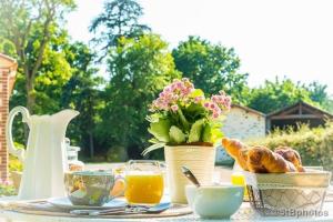 a table with a breakfast of coffee and croissants and flowers at Chambre d'Hôtes La Maisonnette in Étusson
