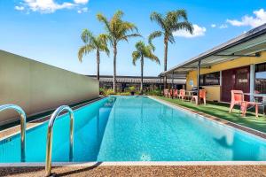 a swimming pool with palm trees and a building at Comfort Inn & Suites Manhattan in Adelaide