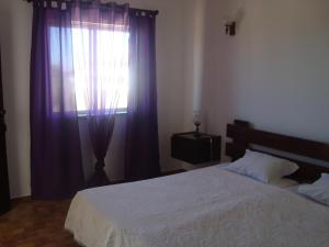 a bedroom with a bed and a window with purple curtains at Mira Fortaleza in Sagres