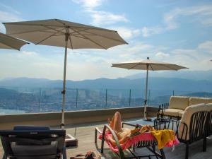 een vrouw op een stoel op een balkon met een paraplu bij Apartment Aldesago Monte Brè - Utoring-28 by Interhome in Viganello