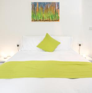 a white bed with a green blanket and a painting on the wall at The Tiger Inn in Merthyr Tydfil