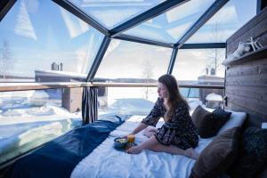 a woman sitting on a bed in a glass house at Ranua Resort Arctic Igloos in Ranua