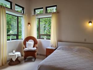 a bedroom with a bed and a chair and windows at Villa Corazón - private beach at Lake Arenal in Nuevo Arenal