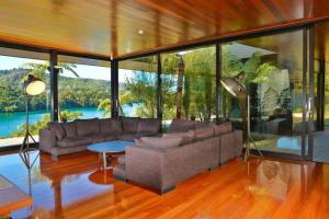 a living room with a couch and a table and windows at Waterfall Bay Glass House in Picton