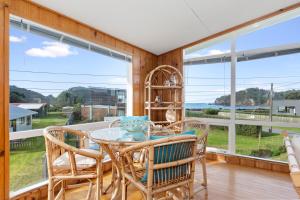 a dining room with a table and chairs and large windows at Matapouri Magic - Matapouri Holiday Home in Matapouri