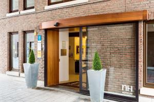 an open door to a brick building with two potted plants at NH Mechelen in Mechelen