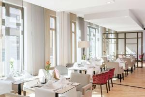 a restaurant with white tables and chairs and windows at NH Collection Nürnberg City in Nuremberg