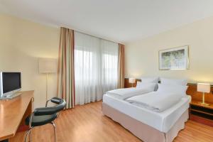um quarto de hotel com uma cama, uma secretária e uma televisão em NH München City Süd em Munique