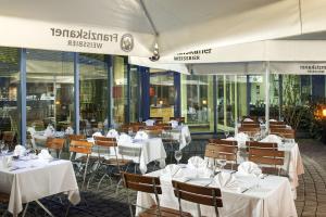 ein Restaurant mit weißen Tischen und Stühlen und Fenstern in der Unterkunft NH München Messe in München + 37 Fotos