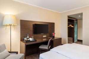 um quarto de hotel com uma secretária com uma televisão e uma cama em NH Stuttgart Airport em Filderstadt