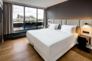 a large white bed in a room with a large window at NH Amsterdam Caransa in Amsterdam
