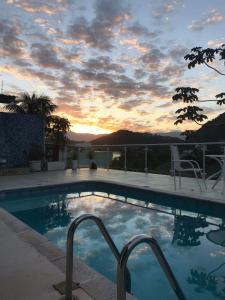 a swimming pool with a sunset in the background at Sua casa in Angra dos Reis