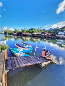 dos personas sentadas en un muelle con barcos en el agua en Watercolours en Ko Chang