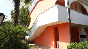 a house with an orange door and palm trees at Residence Leopardi - Gemini in Bibione