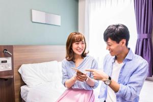 Um homem e uma mulher numa cama a olhar para um telemóvel. em Comfort Hotel Toyokawa em Toyokawa