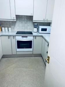 La cuisine est équipée de placards blancs et d'un four avec plaques de cuisson. dans l'établissement Service Apartment, à Thamesmead