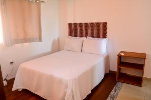 a bedroom with a white bed with a night stand at Flat AGC in Morro de São Paulo