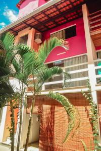 a pink building with palm trees in front of it at Flat AGC in Morro de São Paulo