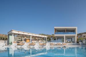 a swimming pool with white chairs and a building at Hermes Grand Luxury Beachfront Villa & Spa, By ThinkVilla in Skaleta