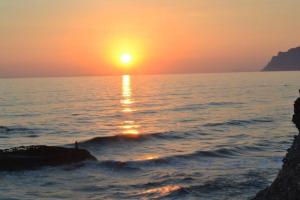 a person standing on a rock in the ocean at sunset at Agathi Beach House (Black Rocks) in Agios Gordios