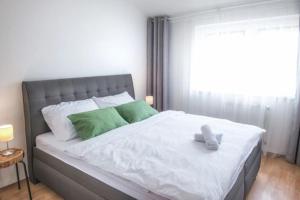 a bed with white sheets and green pillows and a window at Apartmány MINATA in Liptovský Mikuláš