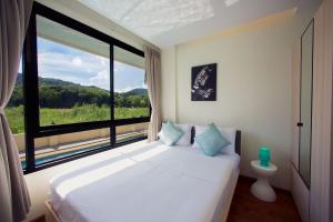 ein Schlafzimmer mit einem Bett und einem großen Fenster in der Unterkunft LAGO APARTMENTS BY TROPICLOOK in Nai Harn Beach