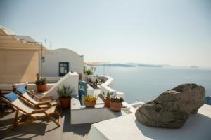 a balcony with chairs and a rock and the water at Gabbiano Traditional Cave Houses in Oia