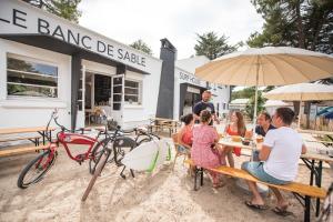 un grupo de personas sentadas en una mesa bajo un paraguas en Dortoir de charme 12 lits 600m plage en Longeville-sur-Mer