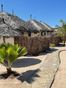 a building with a straw roof and a palm tree at Mambrui Golden Beach Bar and Cottages in Mambrui