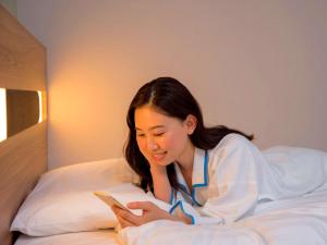 a young girl sitting on a bed reading a book at Comfort Hotel Nara in Nara