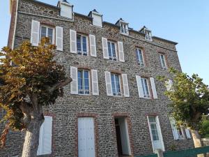 a large brick building with white windows and a tree at Studio cosy au bord de mer in Lancieux