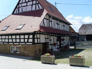 um grande edifício com um telhado vermelho com dois vasos de flores em Gîtes et chambres d'hôtes Maison Ungerer em Hunspach