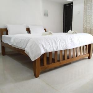 Cama de madera con sábanas y almohadas blancas en Maria Guest House, en Palolem