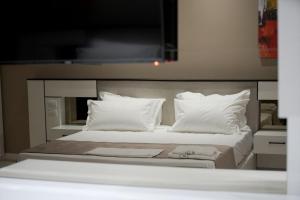 een groot bed met witte kussens en een televisie aan de muur bij Admiral Hotel in Elbasan