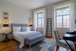 a bedroom with a bed and a chair and two windows at Casa do Cativo in Porto
