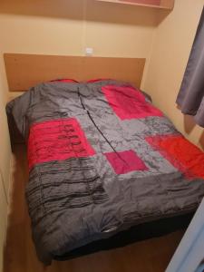 a bed with a red and grey comforter on it at Camping de la mothe in Banassac