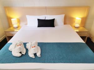 two white teddy bears laying on top of a white bed at Coconut Grove Holiday Apartments in Darwin