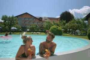 a man and woman sitting in a swimming pool with drinks at Hotel Pachernighof in Velden am Wörthersee
