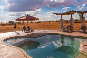 a swimming pool with chairs and an umbrella at Kalahari Anib Camping2Go in Mariental