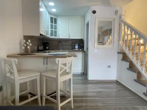 une cuisine avec des placards blancs, un comptoir et des chaises dans l'établissement Apartamento Gustamar 11, à Caleta de Fuste
