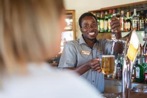 a man standing behind a bar holding a glass of beer at Palmwag Camping2Go in Palm